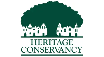 Logo of Heritage Conservancy featuring a large green tree silhouette above a row of white historic building outlines.